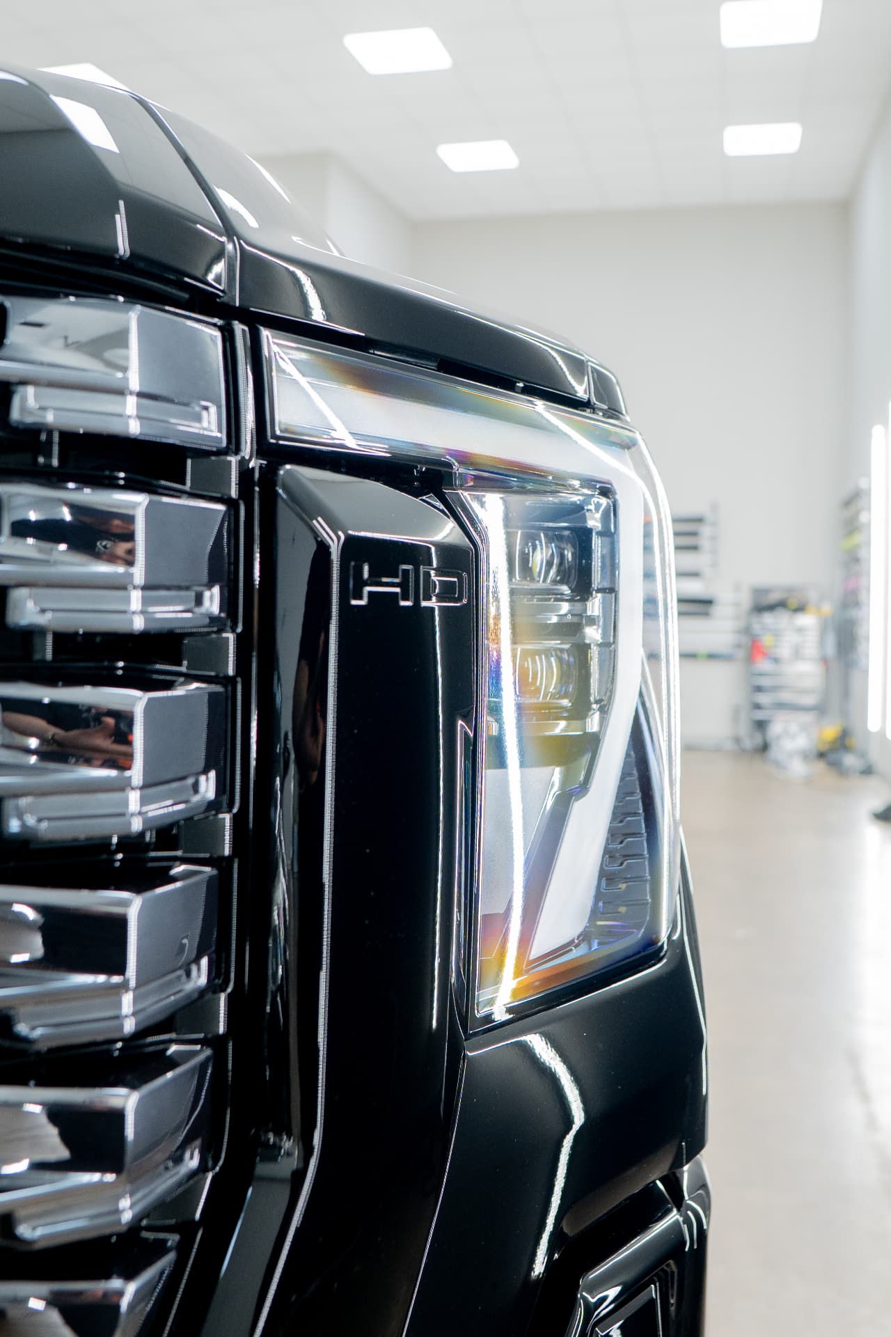 Close-up of a gloss-black GMC Denali HD headlight and grille after paint protection